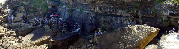 o grupo de ciclistas com as bicicletas s costas a atravessar um monte de pedras