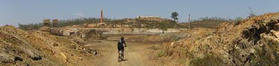ciclista a pedalar com as estruturas abandonadas da mina ao fundo